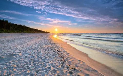 Zachód słońca nad morzem, piaszczysta plaża z odciskami stóp, las w tle. Idealne, fajne miejsce nad morzem dla dwojga na romantyczny spacer.
