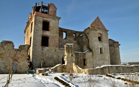 Kamienne ruiny dawnego monastyru w zimowej scenerii. Widać zniszczone mury, łuki okienne i wieżę z platformą widokową.