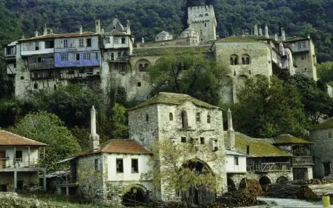 Kamienne budynki klasztorne na zboczu góry Athos, z niebieskim akcentem na jednym z nich.