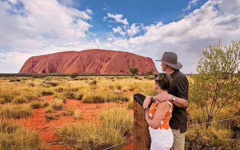 Para turystów podziwia Uluru, świętą skałę rdzennych mieszkańców Australii, w pustynnym krajobrazie.