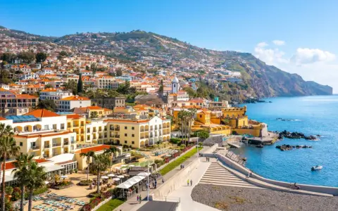 Widok na Funchal, stolicę Madery, z kolorowymi budynkami wznoszącymi się na zboczu góry, otoczonymi błękitnym oceanem.
