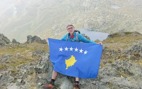 Mężczyzna z flagą najmłodszego państwa Europy, Kosowa, na szczycie góry.