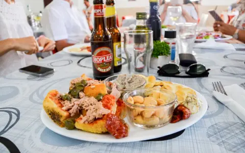 Malta jedzenie: talerz pełen smakołyków z tuńczykiem, fasolą i oliwkami, obok piwo i ludzie przy stole.