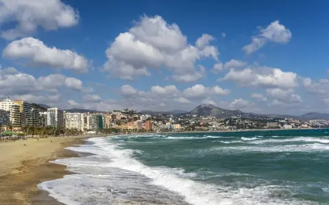 Malaga plaże z falami rozbijającymi się o brzeg i miastem w tle.