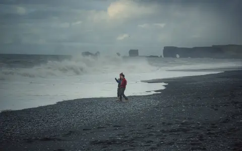 Para spaceruje po czarnej plaży Islandii, podczas gdy fale rozbijają się o brzeg.