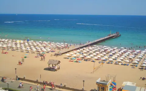 Słoneczny Brzeg, Bułgaria: tłumy plażowiczów, białe parasole, molo i turkusowe morze.