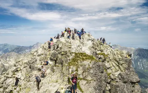 Tłum turystów na skalistym szczycie Rysów, najwyższego szczytu w Polsce, podziwia rozległą panoramę Tatr.