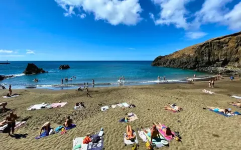 Słoneczne madera plaże z turystami kąpiącymi się w turkusowym oceanie i opalającymi się na piasku.