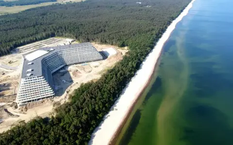Nowy hotel Gołębiewski nad morzem, w otoczeniu lasu sosnowego i szerokiej plaży, z widokiem na turkusowe wody Bałtyku.