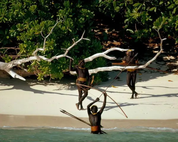 Trzech mężczyzn z plemienia Sentinelese, uzbrojonych w łuki i strzały, stoi na plaży. Sentinel Island, ich dom, chroni ich przed światem.