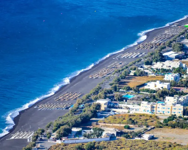 Santorini plaże z czarnym piaskiem, rzędy leżaków i białe budynki hotelowe nad turkusowym morzem.