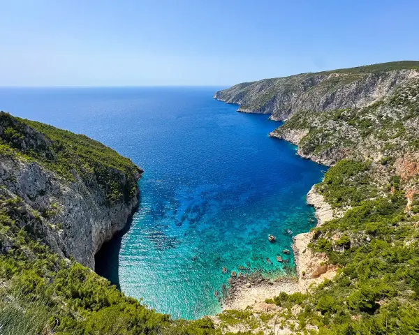 Widok na zatokę z klifami porośniętymi zielenią. Idealne miejsce na zakynthos wycieczki fakultatywne, by podziwiać turkusową wodę.
