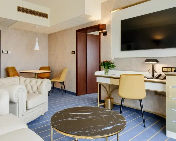 Elegancki pokój w hotelu Diament Wrocław: biała sofa, złote krzesła, biurko z telefonem i kwiatami, stolik kawowy.