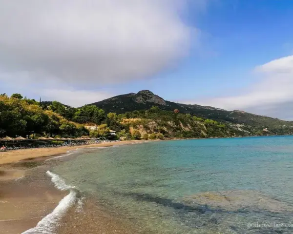 Piękna plaża Tragaki Zakynthos z turkusową wodą, zielonymi wzgórzami i rzędem leżaków pod parasolami.