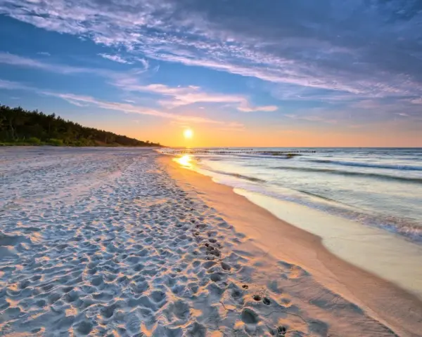 Zachód słońca nad morzem, piaszczysta plaża z odciskami stóp, las w tle. Idealne, fajne miejsce nad morzem dla dwojga na romantyczny spacer.