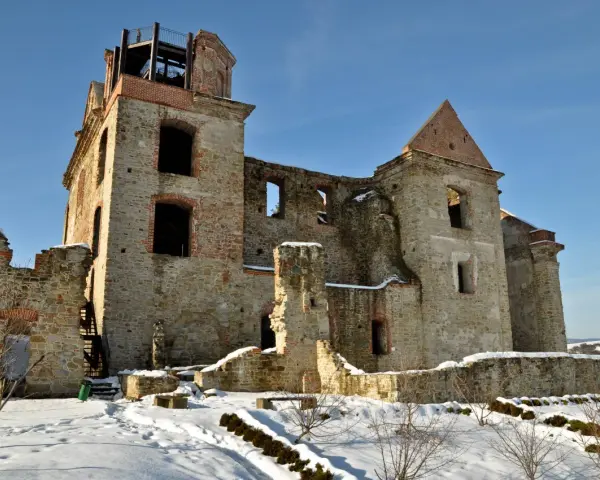 Kamienne ruiny dawnego monastyru w zimowej scenerii. Widać zniszczone mury, łuki okienne i wieżę z platformą widokową.