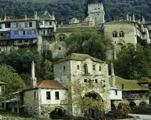 Kamienne budynki klasztorne na zboczu góry Athos, z niebieskim akcentem na jednym z nich.