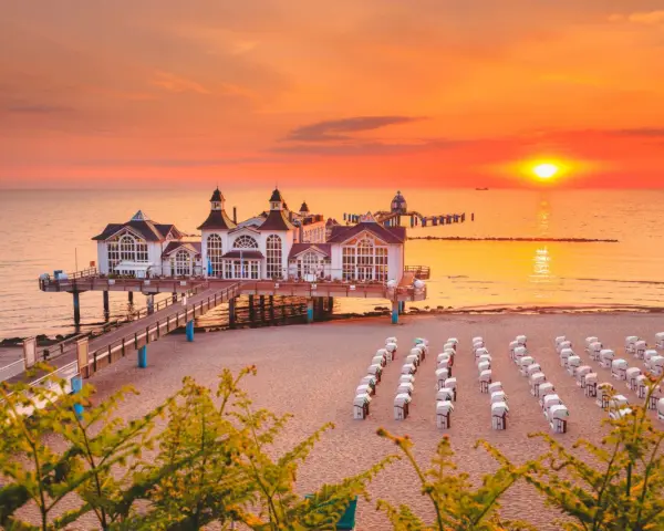 Zachód słońca nad molo w Sellin, na Rugii, największej wyspie Niemiec. Puste kosze plażowe czekają na gości.