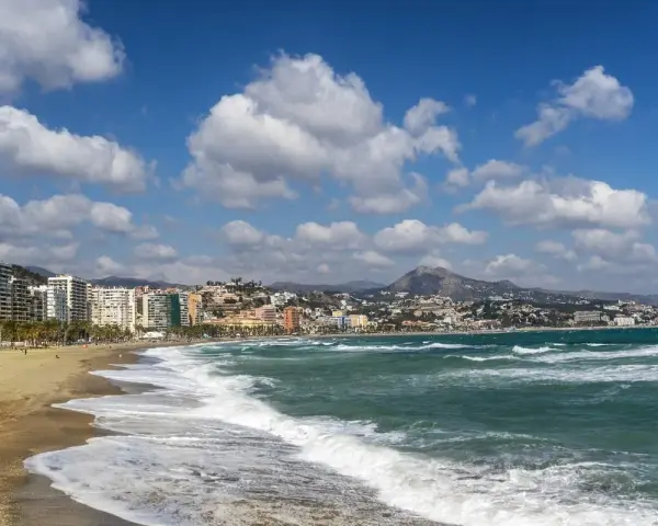 Malaga plaże z falami rozbijającymi się o brzeg i miastem w tle.
