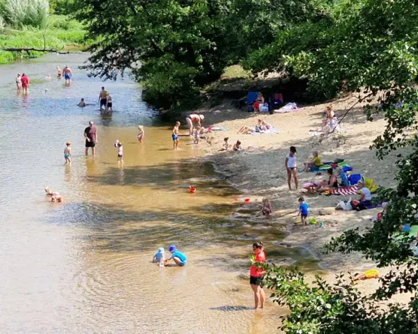 Słoneczny dzień nad Świdrem. Ludzie odpoczywają na piaszczystej plaży i kąpią się w rzece. Dzieci bawią się w wodzie.