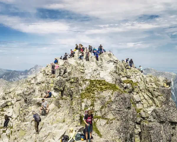 Tłum turystów na skalistym szczycie Rysów, najwyższego szczytu w Polsce, podziwia rozległą panoramę Tatr.