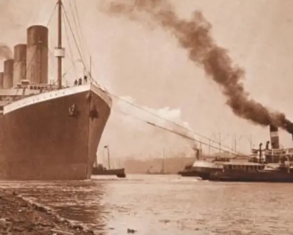 Ogromny statek, prawdopodobnie **Titanic**, wypływa z portu, holowany przez mniejsze jednostki. Dym unosi się z kominów.