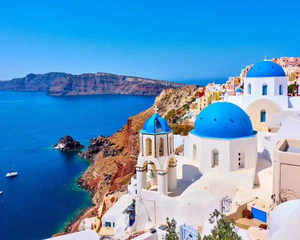 Santorini wakacje: białe domy z niebieskimi kopułami na tle turkusowego morza i klifów. Idealne miejsce na wymarzone wakacje.