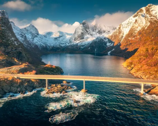 Mosty łączące wyspy w fiordach Norwegii, z ośnieżonymi górami w tle.