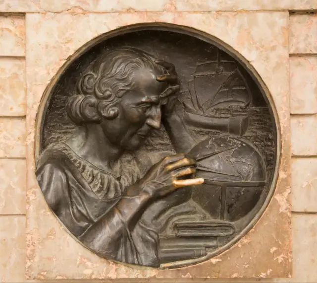 Krzysztof Kolumb, badający mapy i globus, symbolizuje jego pochodzenie i dążenie do odkryć. W tle żaglowiec.