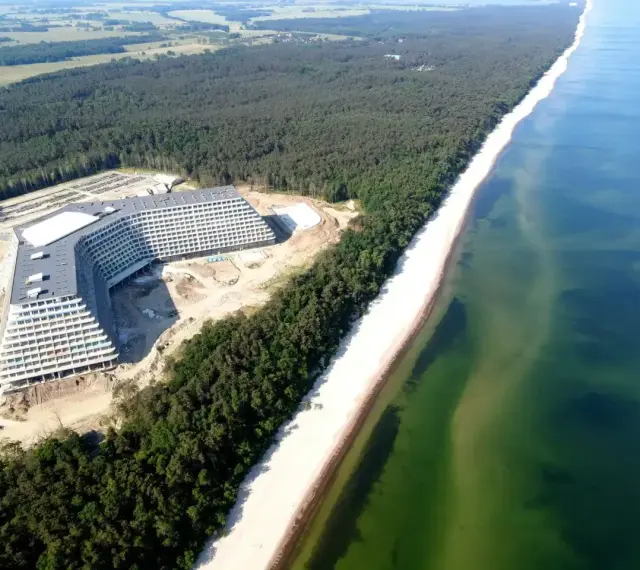 Nowy hotel Gołębiewski nad morzem, w otoczeniu lasu sosnowego i szerokiej plaży, z widokiem na turkusowe wody Bałtyku.