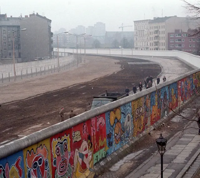 Kolorowy mur berliński, symbol zburzenia muru berlińskiego, z ludźmi i ciężarówką w tle.