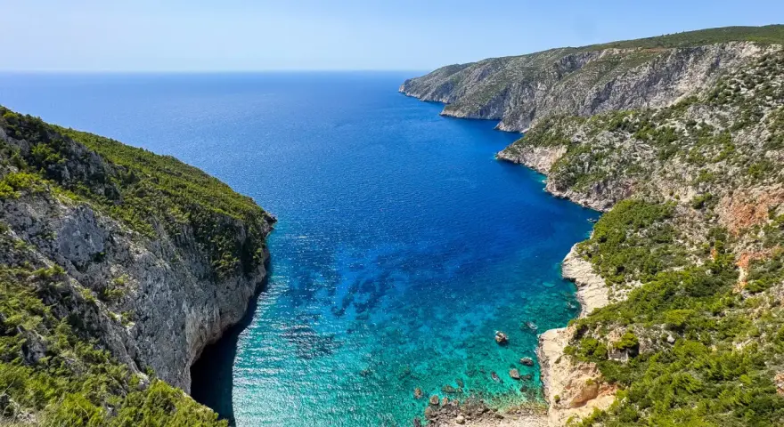 Widok na zatokę z klifami porośniętymi zielenią. Idealne miejsce na zakynthos wycieczki fakultatywne, by podziwiać turkusową wodę.