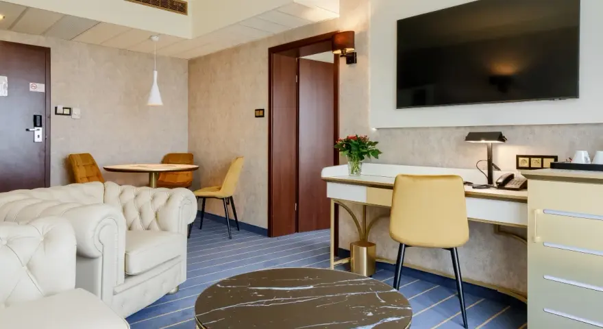 Elegancki pokój w hotelu Diament Wrocław: biała sofa, złote krzesła, biurko z telefonem i kwiatami, stolik kawowy.