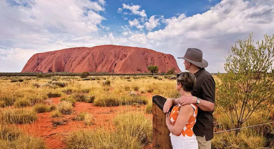 Para turystów podziwia Uluru, świętą skałę rdzennych mieszkańców Australii, w pustynnym krajobrazie.