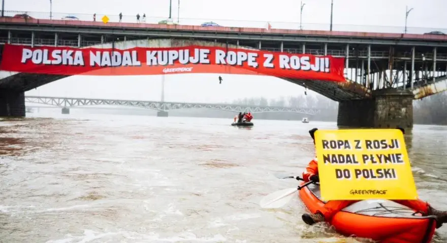 Na moście Poniatowskiego wisi czerwony baner "Polska nadal kupuje ropę z Rosji!". Kajakarz Greenpeace na Wiśle trzyma żółtą tablicę "Ropa z Rosji nadal płynie do Polski".