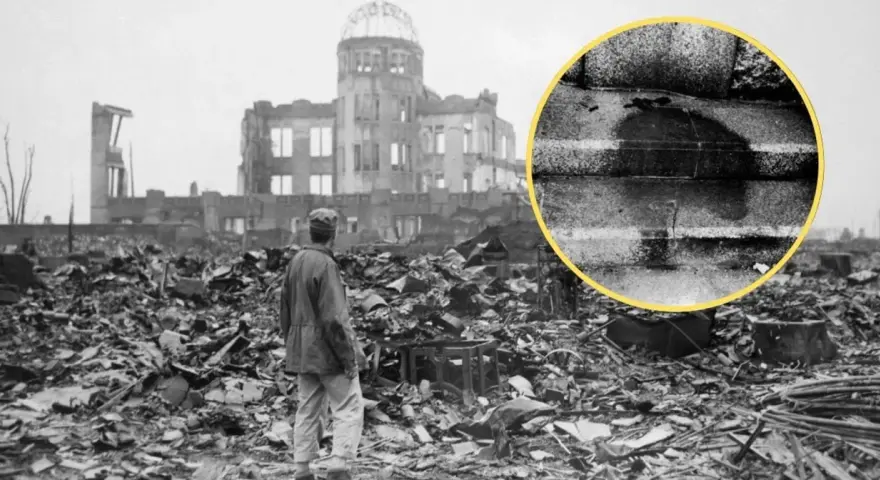 Ruiny w Hiroszimie po bombardowaniu atomowym. W oddali widać zniszczony budynek, a na pierwszym planie stos gruzów i stojącego człowieka. W kółku widoczny ślad po ciele.