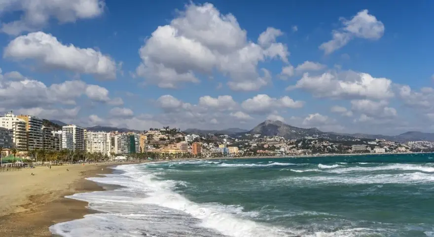 Malaga plaże z falami rozbijającymi się o brzeg i miastem w tle.