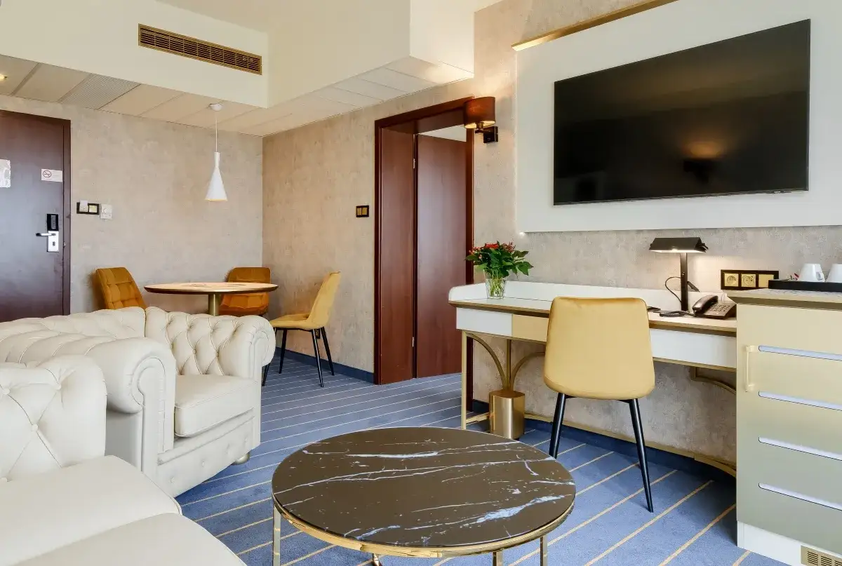 Elegancki pokój w hotelu Diament Wrocław: biała sofa, złote krzesła, biurko z telefonem i kwiatami, stolik kawowy.
