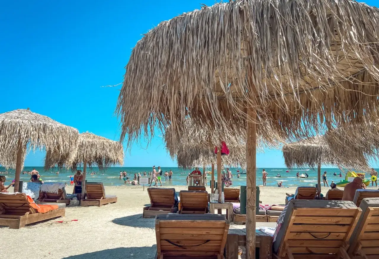 Słoneczne plażowe leżaki i parasole z trawy morskiej, idealne na rumuńskie wakacje. Ludzie kąpią się i relaksują w morzu.