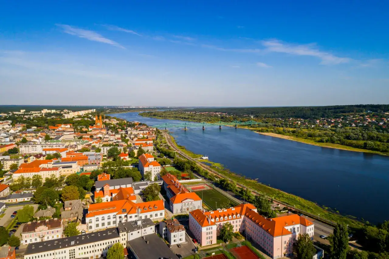 Widok na miasto i szeroką rzekę, najdłuższa rzeka w Polsce, z zielonym mostem w oddali.