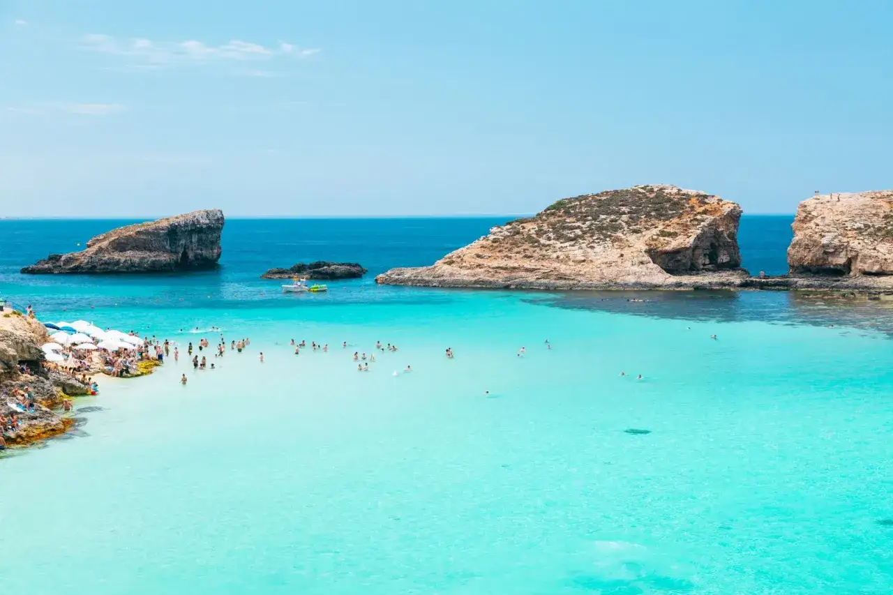 Malta plaże: turkusowa woda, skaliste klify i tłumy ludzi cieszących się słońcem i kąpielą w Zatoce Błękitnej.