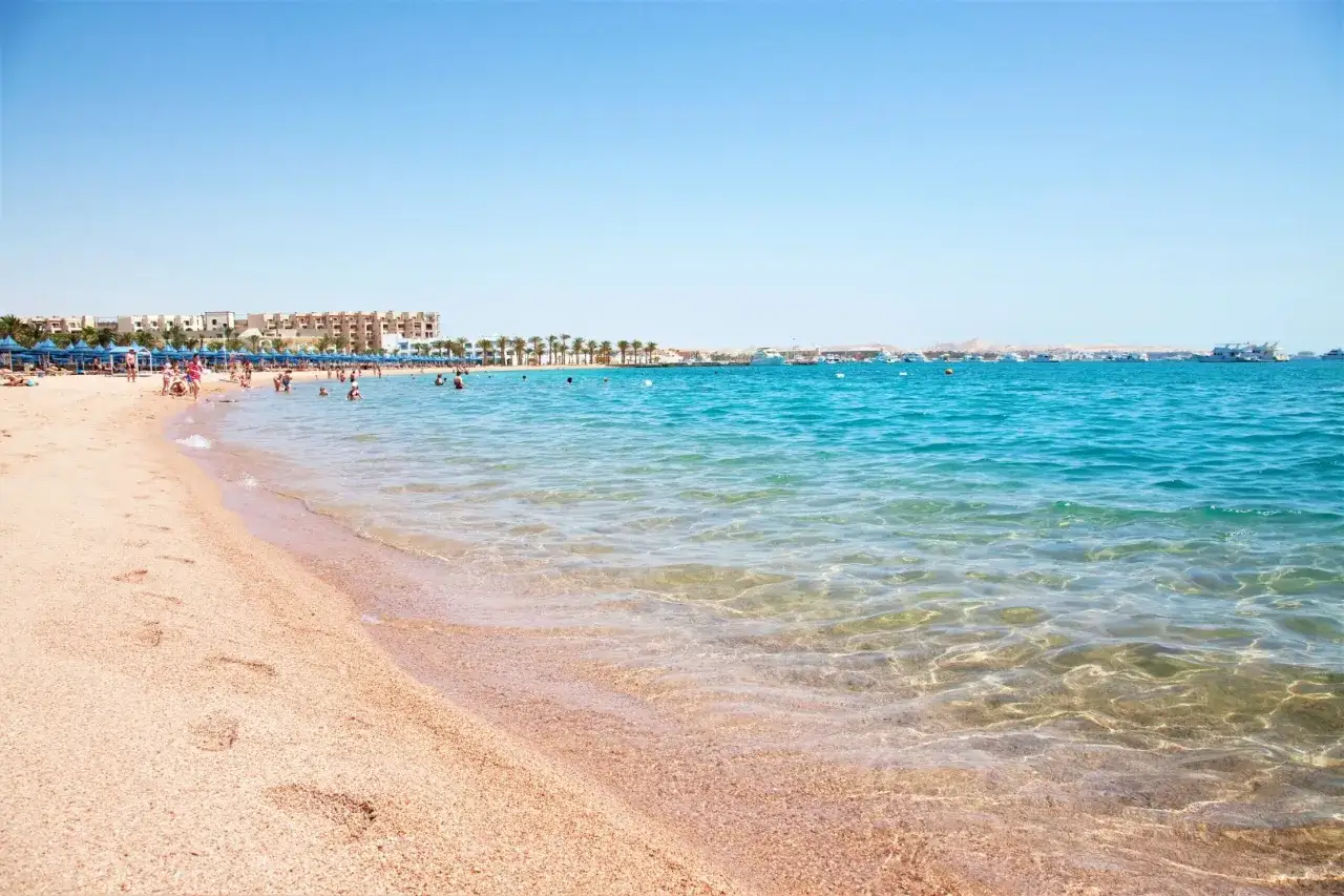 Piasek, turkusowa woda i hotele w Makadi Bay. Ludzie kąpią się i opalają na plaży.