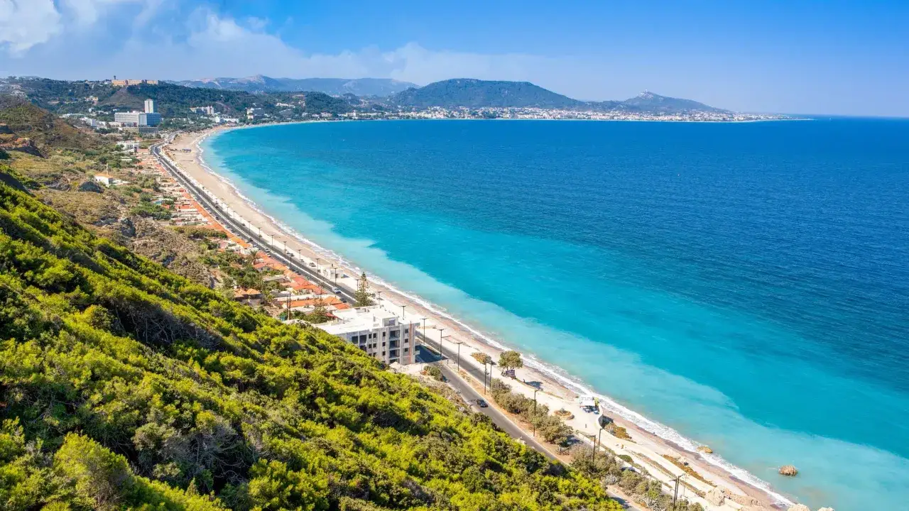 Widok na Ixia, Rodos: turkusowe morze, plaża, droga i zielone wzgórza.