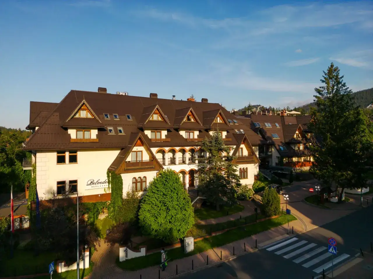 Elegancki hotel Belvedere Resort & Spa w otoczeniu zieleni, z charakterystyczną architekturą i pięknym dachem.