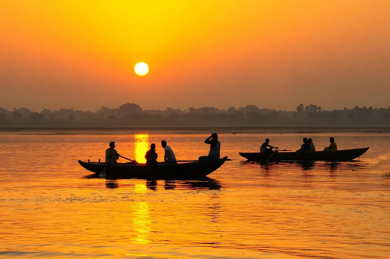Łodzie na rzece Ganges podczas zachodu słońca. Ludzie w łodziach, odbicia słońca na wodzie.