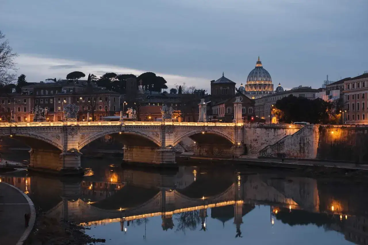 Most znany w Rzymie, Ponte Sant'Angelo, odbija się w spokojnej rzece Tyber. W tle widać kopułę Bazyliki św. Piotra.