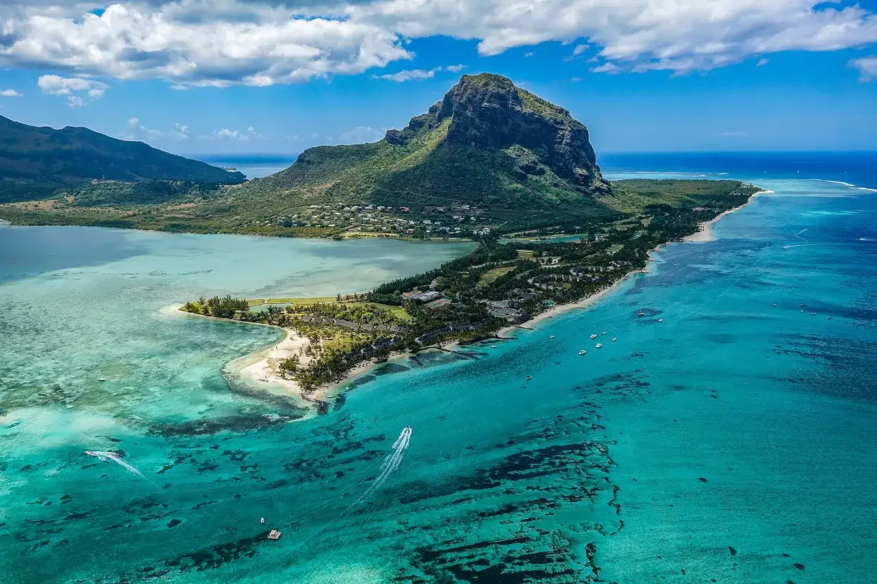 Widok z lotu ptaka na górzysty krajobraz i turkusowe morze, gdzie leży Mauritius. Widać plaże, hotele i łodzie.