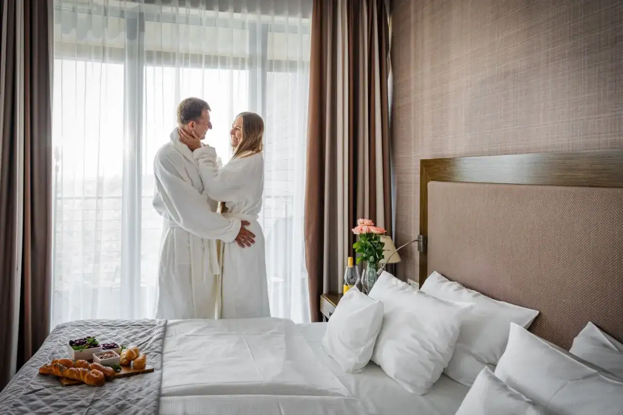 Para dwojga w szlafrokach przy oknie. Romantyczny poranek w hotelu nad morzem, z pysznym śniadaniem na łóżku.