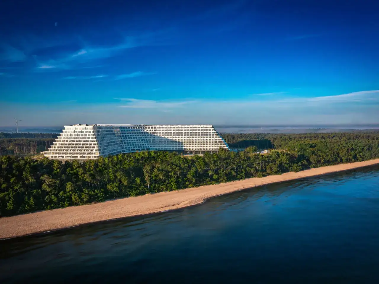 Imponujący hotel Gołębiewski nad morzem, otoczony lasem, z widokiem na piaszczystą plażę i błękitne wody.