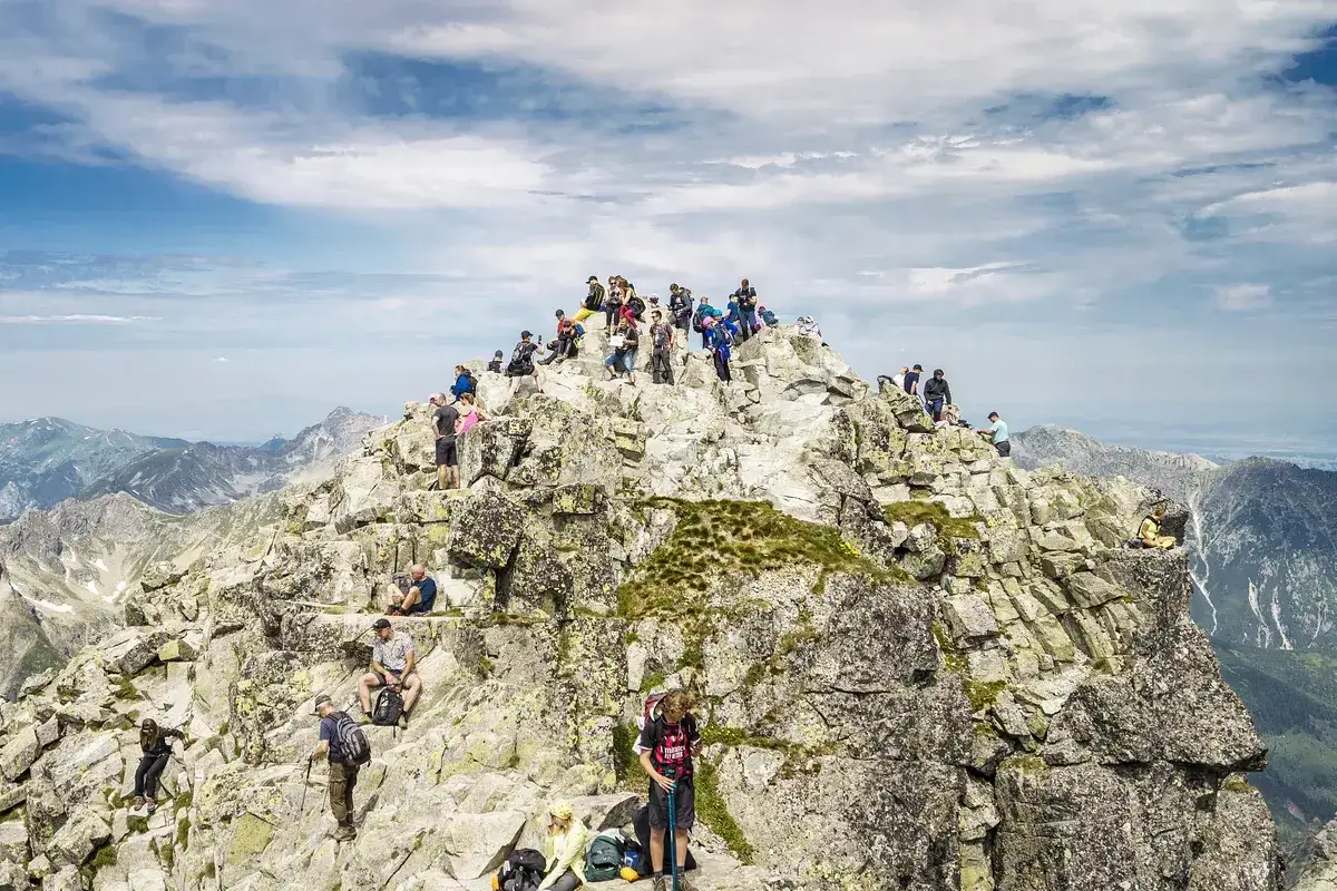 Tłum turystów na skalistym szczycie Rysów, najwyższego szczytu w Polsce, podziwia rozległą panoramę Tatr.